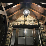 Large Victorian Globe Hanging Lantern on a chain in black, cast iron banded cage over an entrance porch with wood beams and stone walls.