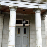 Large Victorian globe hanging lantern in black, cast iron caged sphere on a chain, suspended above a grey panelled front door between two white columns.