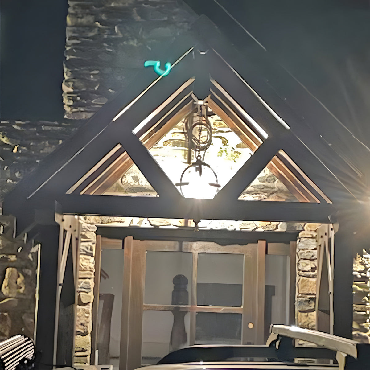 Large Victorian globe hanging lantern in black iron with banded cage, suspended on a chain from a stone-clad gable porch above a wooden entrance door.