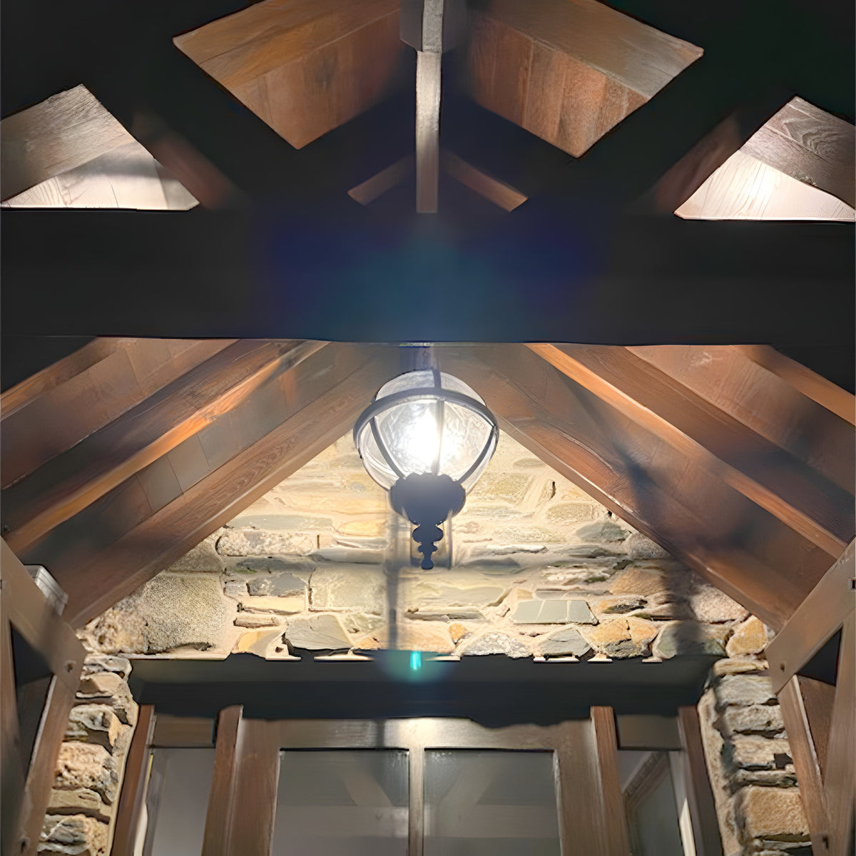 Large Victorian Globe Hanging Lantern in black, cast iron banded cage on a chain, illuminated beneath exposed wood beams and stone archway at an entrance.