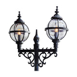 Victorian-style double-headed cast iron lamp post in black, with two clear globe shades in banded cages atop scrolled brackets and a central finial, shown against a plain white background.