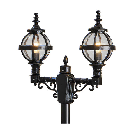 Victorian double-headed lamp post in black cast iron with two globe lanterns in banded cages, decorative scrollwork brackets and finials, shown against a plain white background.