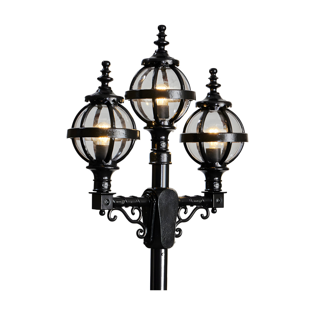 Victorian-style triple-headed lamp post in black cast iron, with three globe lanterns in banded cages and ornate scroll brackets, shown lit against a plain white background.