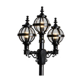 Victorian-style triple-headed lamp post in black cast iron, with three globe lanterns in banded cages and ornate scroll brackets, shown lit against a plain white background.