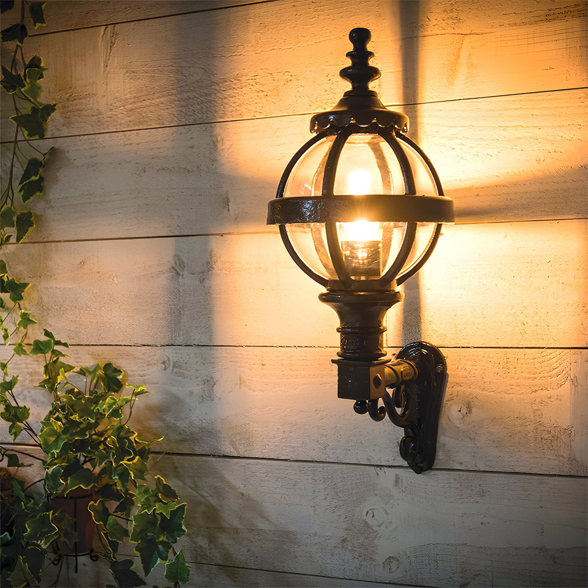 Small Victorian Globe Wall Lantern in black, cast iron cage design on a scroll bracket, mounted on a wooden panelled wall with warm lit glass globe, IP44 rated for outdoor use.