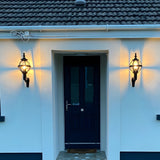Small Victorian Globe Wall Lantern in black, mounted on a scroll bracket either side of a navy front door, illuminated on a white house exterior.