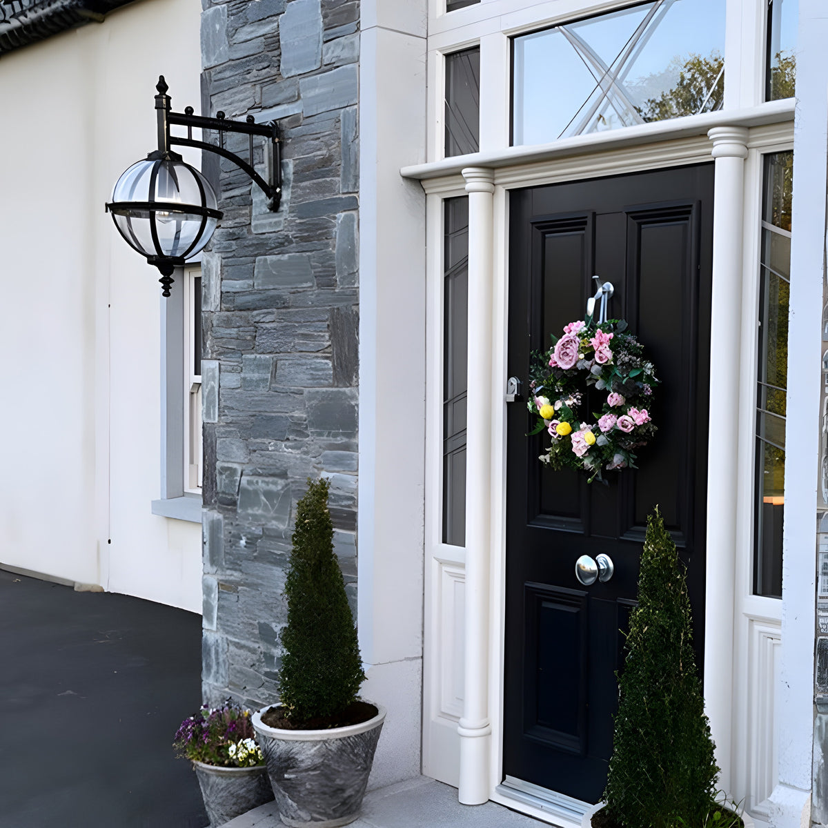 Large Victorian downturned globe wall lantern in black cast iron with clear polycarbonate glazing, mounted on a grey stone pillar beside a black front door.