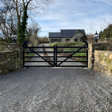 Medium Victorian Globe Pillar Light in black, mounted on stone gate piers flanking a driveway with black metal gates leading to a house.
