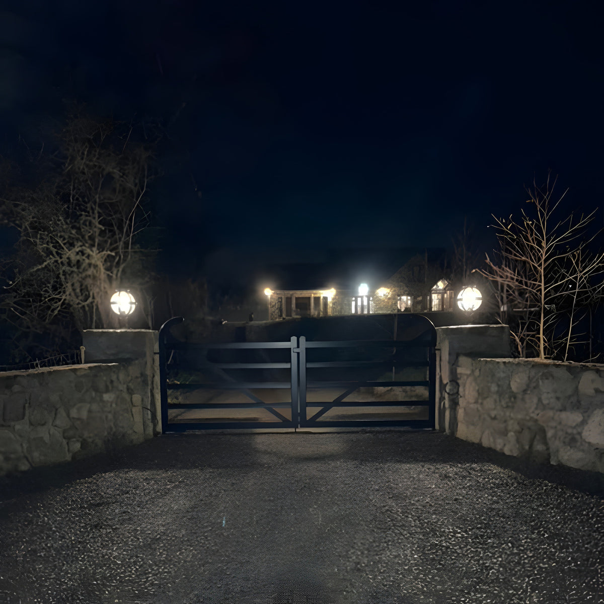 Medium Victorian Globe Pillar Light for Flat Piers in black, mounted on stone gate piers either side of a driveway gate, illuminated at night.