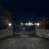 Medium Victorian Globe Pillar Light for Flat Piers in black, mounted on stone gate piers either side of a driveway gate, illuminated at night.