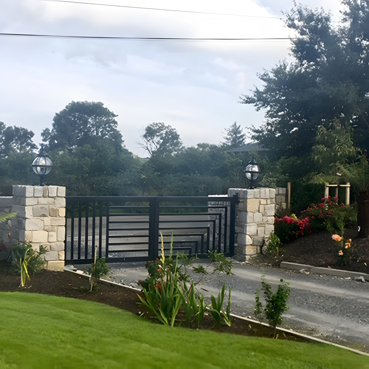 Medium Victorian Globe Pillar Light in black mounted on stone gate piers, showing the round glass globe in a banded cage above a turned cast base, flanking an entrance gate.