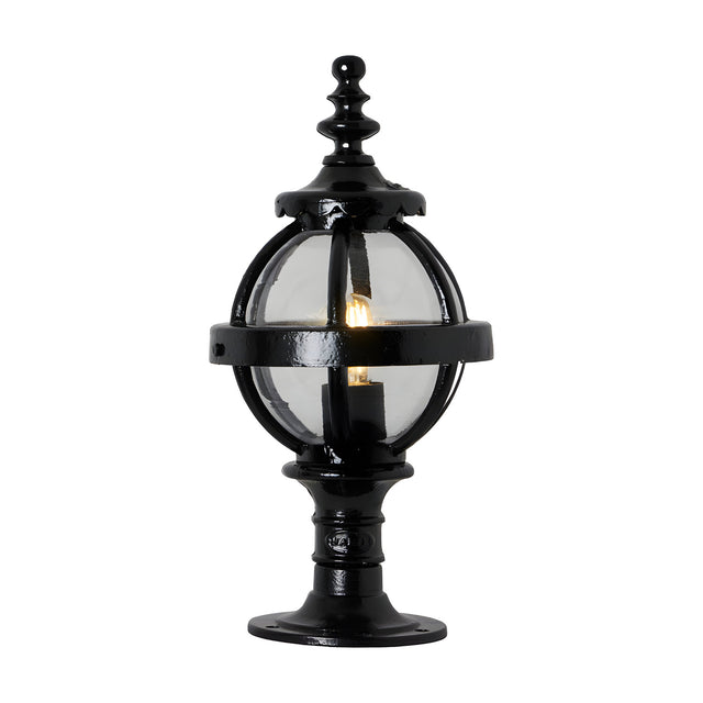 Small Victorian Globe Pillar Light in black, cast iron banded cage with clear glass globe on a decorative pedestal base, lit bulb visible, plain white background.