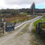 Small Victorian Globe Pillar Light in black mounted on stone gate piers, illuminating a gravel driveway with pathway lighting and a gated entrance.