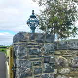Small Victorian Globe Pillar Light in black metal with caged glass globe, mounted on a stone pier cap beside a keypad entry unit and gate.