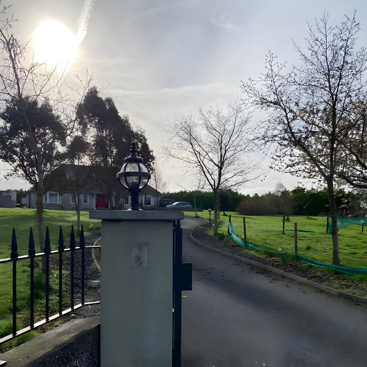 Small Victorian Globe Pillar Light in black, cast iron banded cage design, mounted on a flat pier cap at a garden entrance driveway.