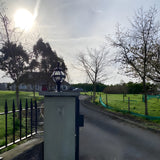 Small Victorian Globe Pillar Light in black, cast iron banded cage design, mounted on a flat pier cap at a garden entrance driveway.