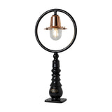 Small railway-style cast iron pedestal post light with a black circular hoop frame, copper spun shade over a clear glass dome, ribbed black base, on a plain white background.