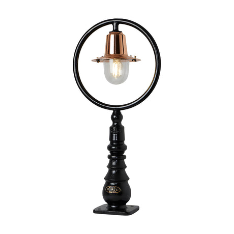 Small railway-style cast iron pedestal post light with a black circular hoop frame, copper spun shade over a clear glass dome, ribbed black base, on a plain white background.