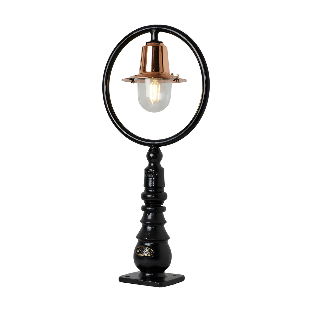 Small railway-style cast iron pedestal post light with black circular hoop frame, copper spun shade, clear glass dome, and stepped iron base on a plain white background.