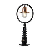 Small railway-style cast iron pedestal post light with black circular hoop frame, copper spun shade, clear glass dome, and stepped iron base on a plain white background.