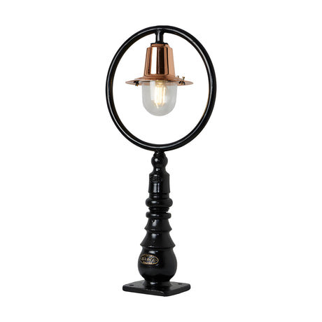 Small railway-style cast iron pedestal post light with black circular hoop frame, copper spun shade, clear glass dome, and stepped iron base on a plain white background.