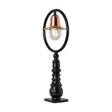 Small railway-style cast iron pedestal post light with black oval hoop frame, copper spun shade over a clear glass dome, on a decorative black base with square mounting plate, plain white background.