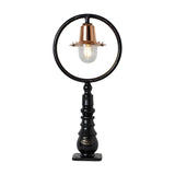 Small railway style cast iron pedestal post light with a black circular hoop frame, copper spun shade, and clear glass dome on a black turned base, plain white background.
