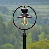 Railway style black cast iron lamp post, 3.65m, with a circular hoop frame around a spun shade and clear glass dome, lit bulb, set outdoors against a rural backdrop.