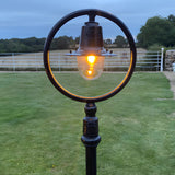 Railway Style Cast Iron Lamp Post, 1.49m, black finish, with a spun shade encircled by a hoop over a glowing polycarbonate dome, set on a garden lawn.