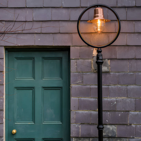 Railway Style cast iron lamp post, 2.43m, black frame with circular hoop, copper spun shade over a lit glass dome, mounted beside a green panelled door on a grey tiled wall.