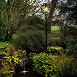 Railway Style Cast Iron Lamp Post in black, 2.43m tall with a lit lantern head under a hoop, set in a lush garden beside a small stream.