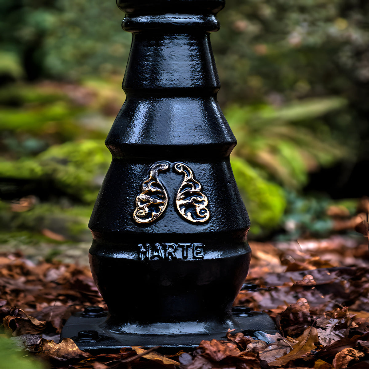 Base of the Railway Style Cast Iron Lamp Post in black, showing a tiered iron column with scroll motif and "HARTE" text, set on fallen autumn leaves outdoors.