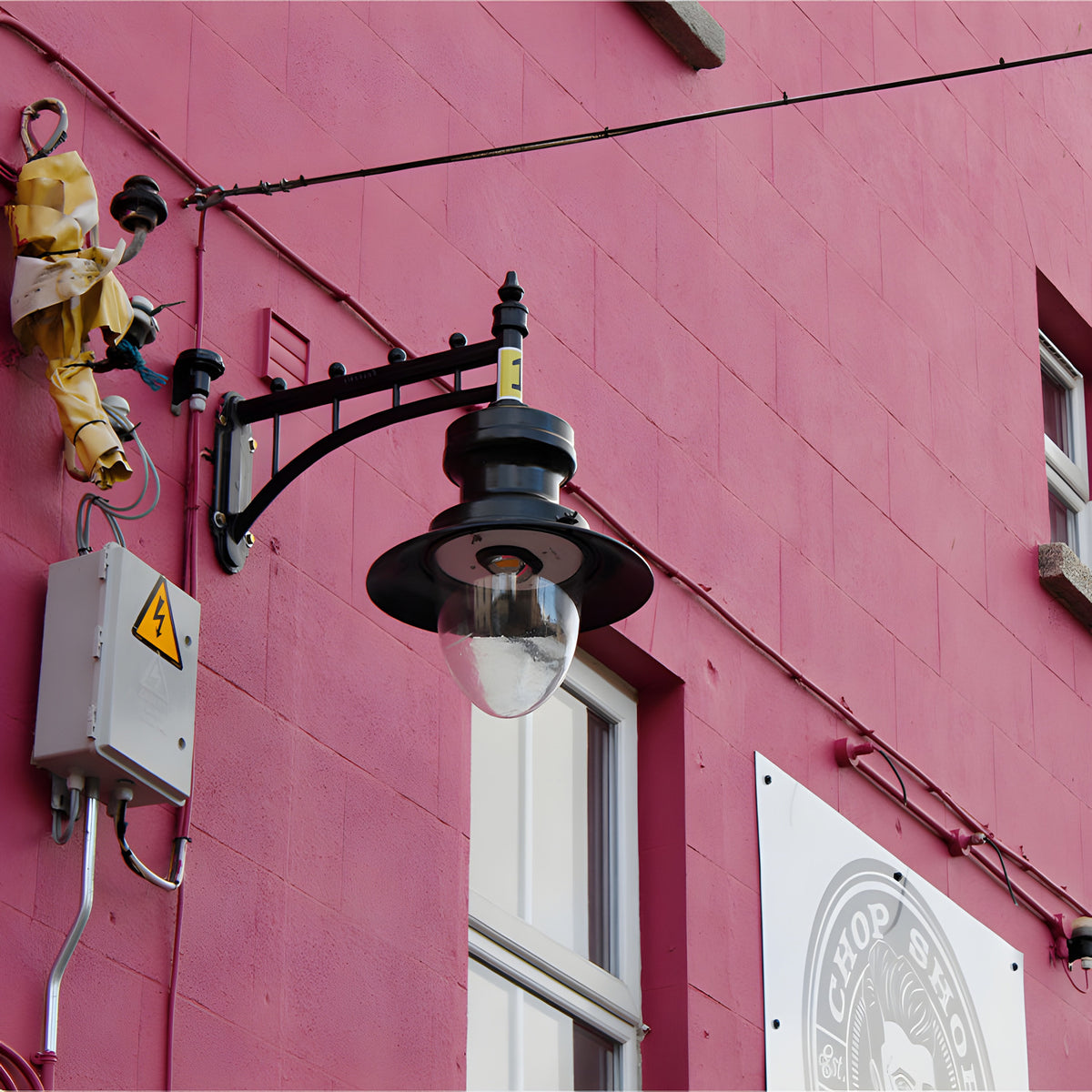 Large railway style wall lantern in black on a trussed cast arm, with a domed clear glass shade, mounted on a pink exterior wall.