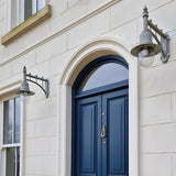 Two Medium Railway Style wall lanterns on cast arms mounted either side of an arched navy front door, grey finish with clear glass domes on a cream stone façade.