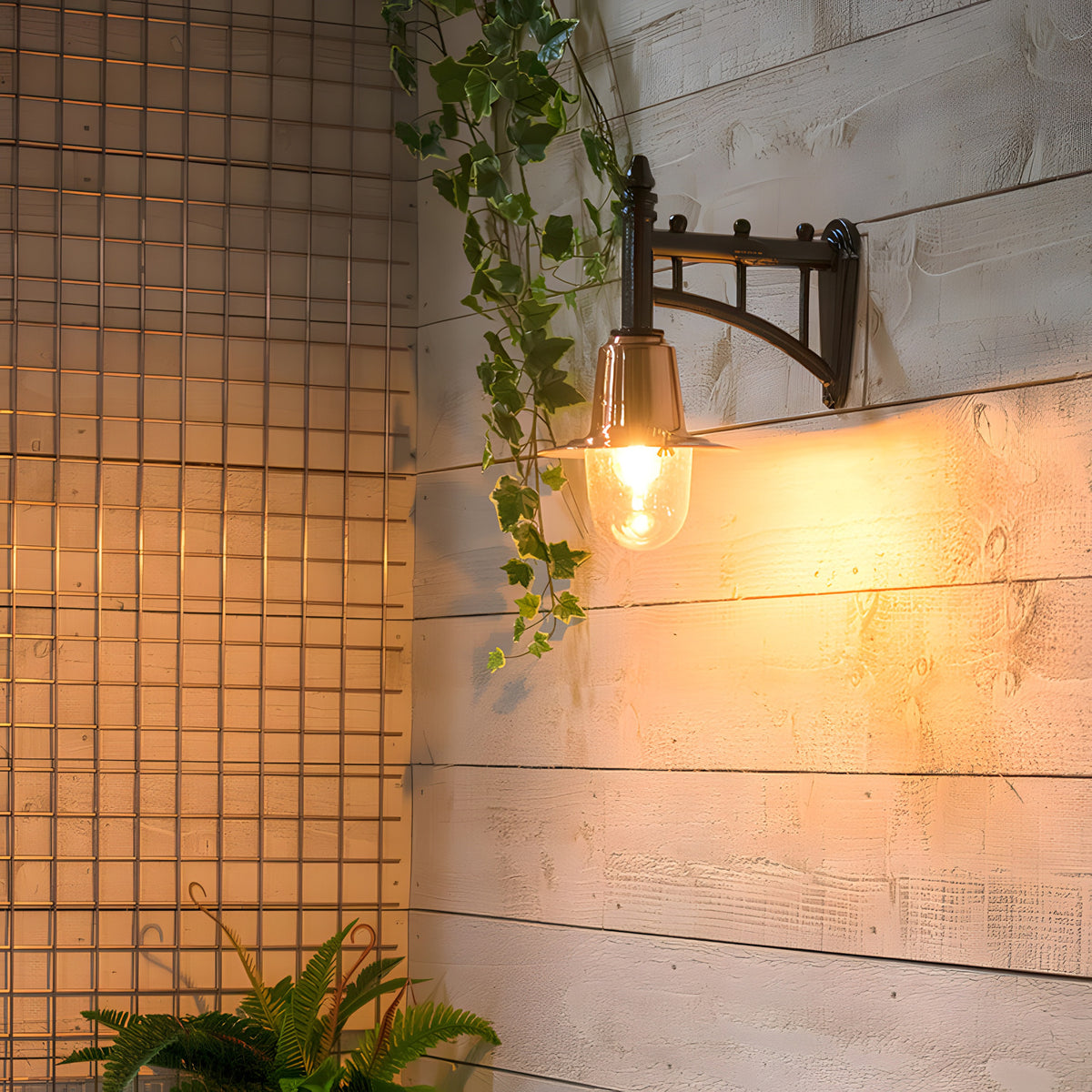 Small Railway Style Wall Lantern on a cast arm with copper shade and clear glass dome, illuminated on a white timber wall beside trailing ivy.