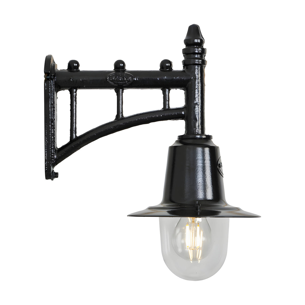 Small railway style black wall lantern on a trussed cast iron arm with a spun metal shade over a clear glass dome and visible bulb, shown on a white background.