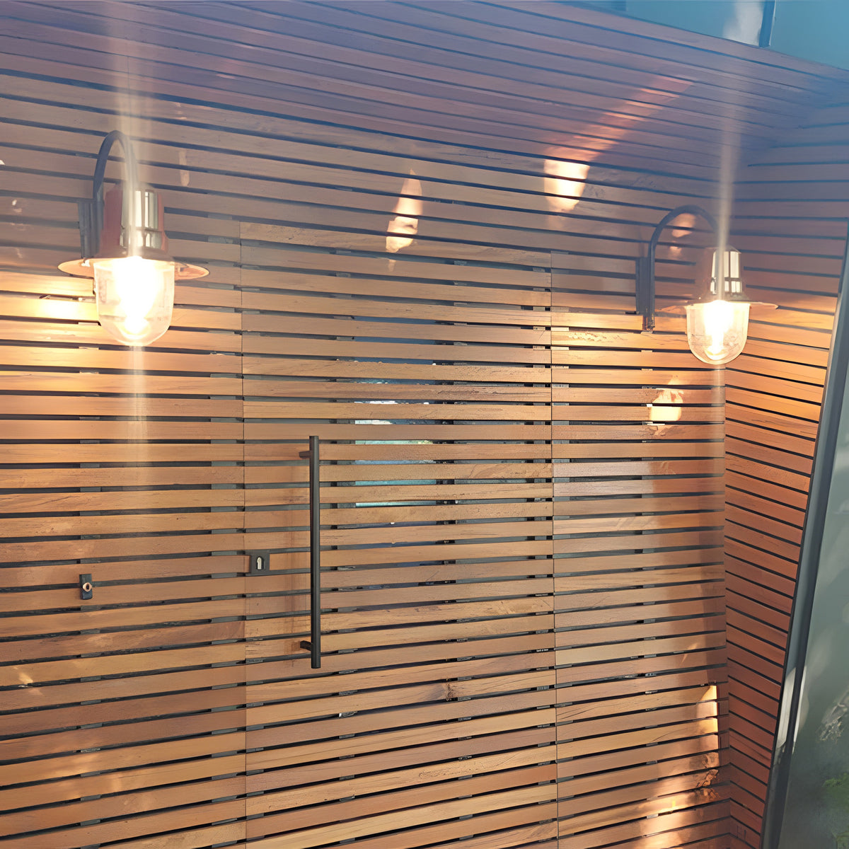 Two Small Vintage Wall Lanterns on gooseneck brackets with copper teardrop shades, mounted on a slatted wood wall either side of a black door handle.