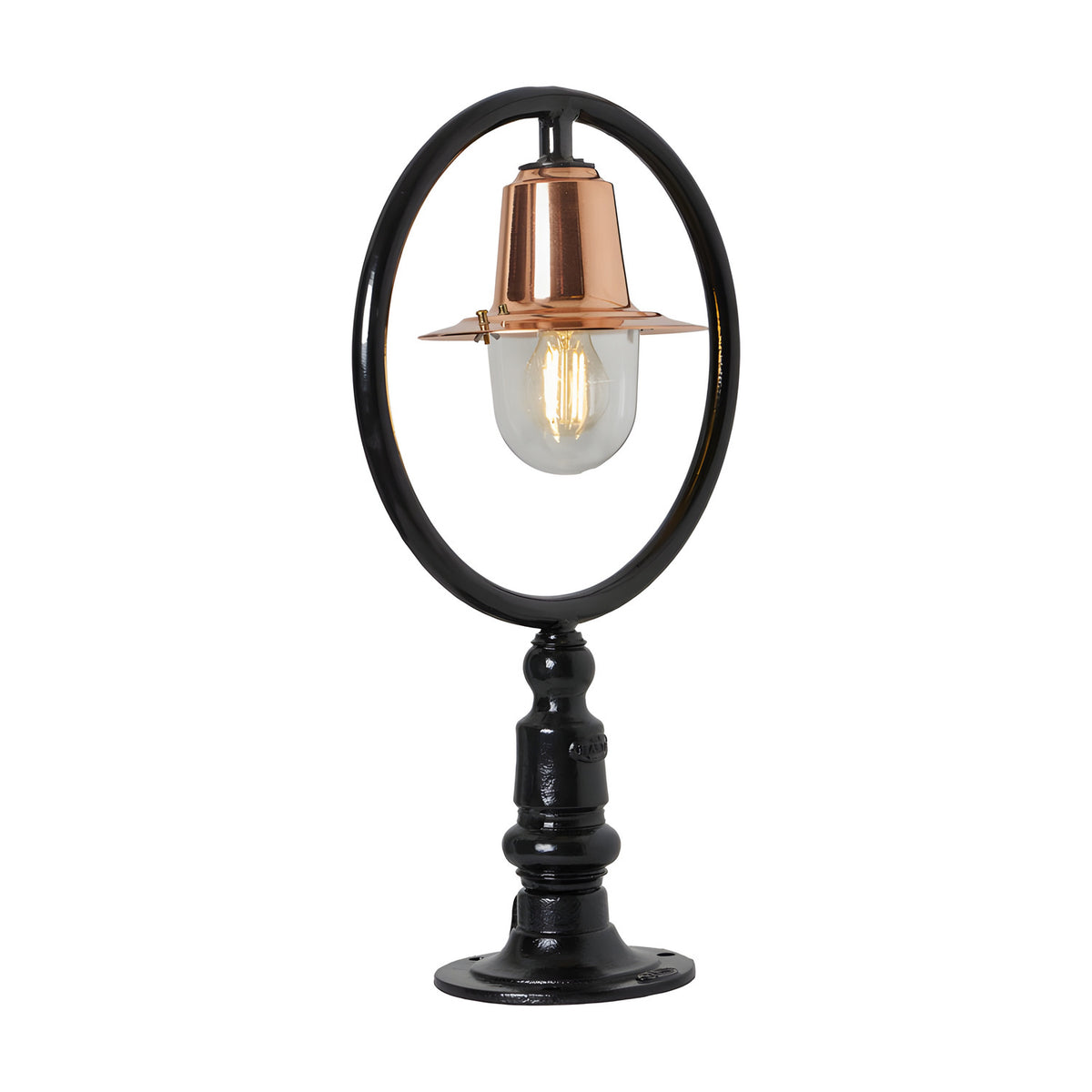 Small railway style pillar light with a black hoop frame, copper spun shade, and clear glass dome on a black cast pier base, plain white background.
