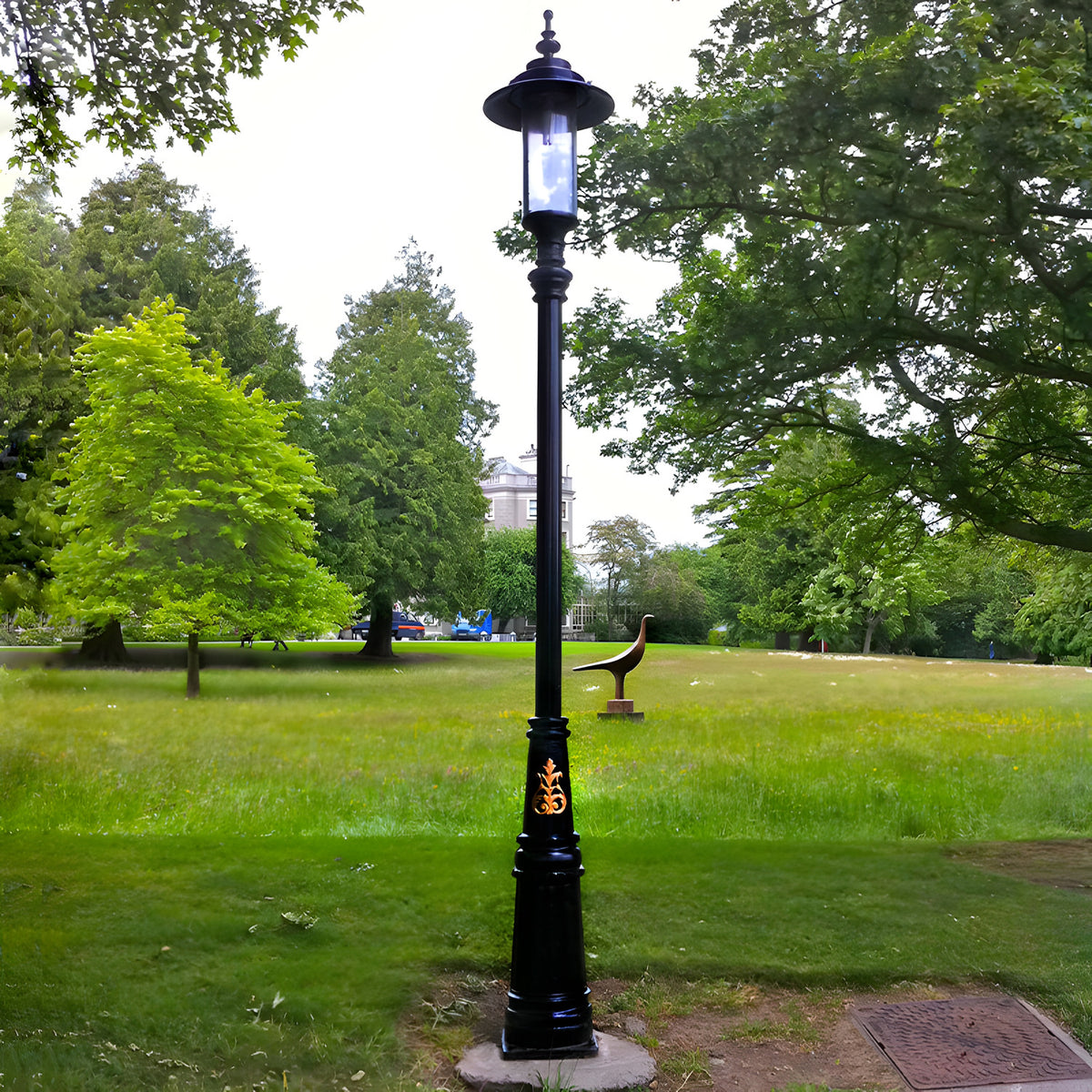 Georgian Cast Iron Lamp Post 3.5m in black, tall traditional style with lantern-style top and decorative gold motif, installed on a paved base in a green parkland setting.