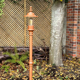 Georgian cast iron lamp post in copper-tone finish with lantern-style head and visible bulb, installed outdoors in a garden setting against a trellis fence and tree.