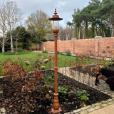 Georgian cast iron lamp post in a terracotta finish, 2.21m tall with a lantern head and glass panel, installed in a garden border beside a brick wall.