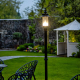 Georgian cast iron lamp post in black, 2.21m tall, single lantern head with clear glass panels, illuminated, standing on a lawn in a garden setting.