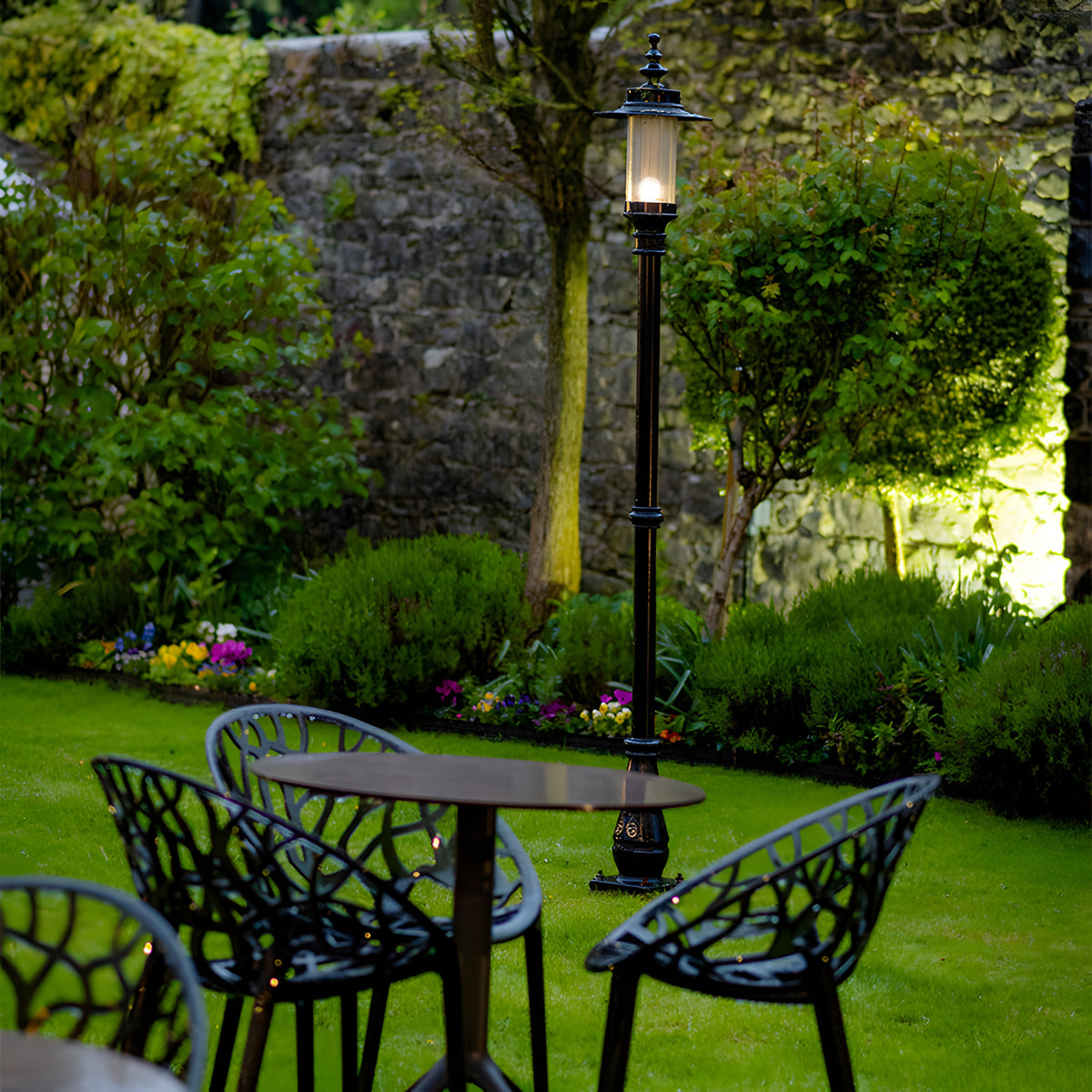 Georgian Cast Iron Lamp Post 2.21m in black, traditional single-light post with lantern head, shown illuminated on a lawn beside a garden table and chairs.