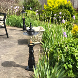 Large Georgian Cast Iron Pedestal Post Light in black, shown lining a garden path amid iris flowers and greenery, with lantern-style glass shade and squared base.
