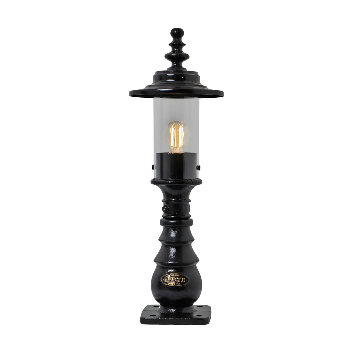 Small Georgian cast iron pedestal post light in black with clear cylindrical glass, decorative crown finial, and square mounting base, shown lit on a plain white background.