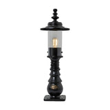 Small Georgian cast iron pedestal post light in black with clear cylindrical glass, decorative crown finial, and square mounting base, shown lit on a plain white background.