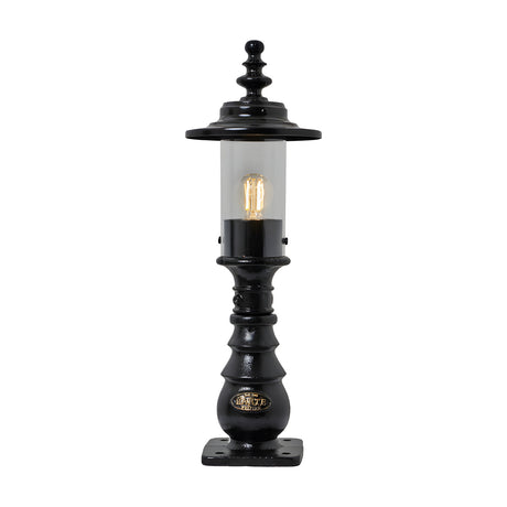 Small Georgian cast iron pedestal post light in black with clear cylindrical glass, decorative crown finial, and square mounting base, shown lit on a plain white background.
