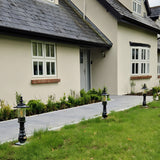 Small Georgian cast iron pedestal post lights in black lining a garden pathway leading to a house entrance, each with a square base and lantern-style glass head.
