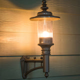 Small Georgian Cast Iron Wall Lantern in black, mounted on wooden cladding with lit bulb, clear cylindrical glass panel, domed crown top and decorative wall bracket.