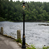 Vintage cast iron lamp post in black with gooseneck curve and teardrop shade over glass dome, shown lit beside a riverside path.